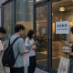 Realistic editorial image of young game fans outside a Beijing venue with an event canceled notice on the door.