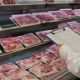 Generic packaged pork in a Chinese supermarket meat case beside a food safety inspection clipboard