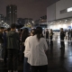 Night-time crowd outside a large warehouse-style retail building in Chongqing with police lights in the distance