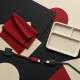 Crimson fabric, an empty meal tray and disconnected cable shapes in a charcoal and ivory paper collage.