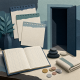 Paper collage of a blank ledger, layered calendar pages, coins, spa stones, a folded towel, and a dark doorway.